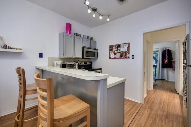 kitchen featuring a breakfast bar, light wood finished floors, light countertops, stainless steel appliances, and baseboards