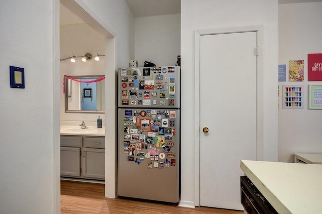 kitchen featuring freestanding refrigerator, a sink, light wood finished floors, and light countertops