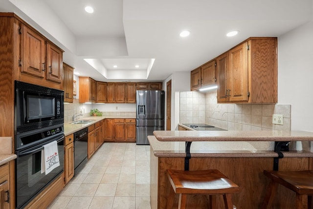 kitchen with recessed lighting, a peninsula, tasteful backsplash, a tray ceiling, and black appliances
