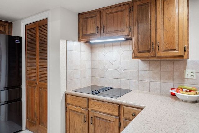 kitchen with backsplash, under cabinet range hood, brown cabinetry, and black appliances