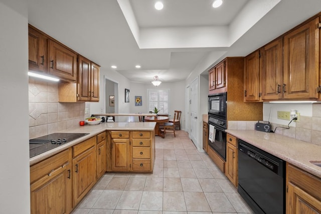 kitchen with light countertops, brown cabinetry, black appliances, and a peninsula