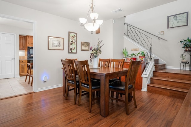 dining area with visible vents, light wood-style floors, baseboards, stairway, and a chandelier