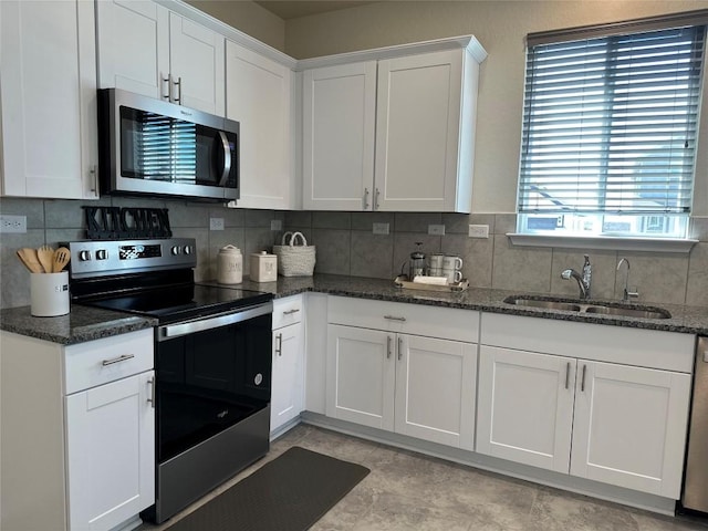 kitchen with white cabinets, appliances with stainless steel finishes, a sink, dark stone countertops, and backsplash