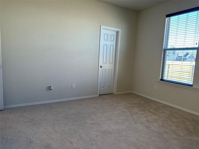 spare room with baseboards, plenty of natural light, and light carpet