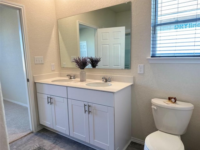 bathroom featuring double vanity, a sink, a textured wall, and toilet