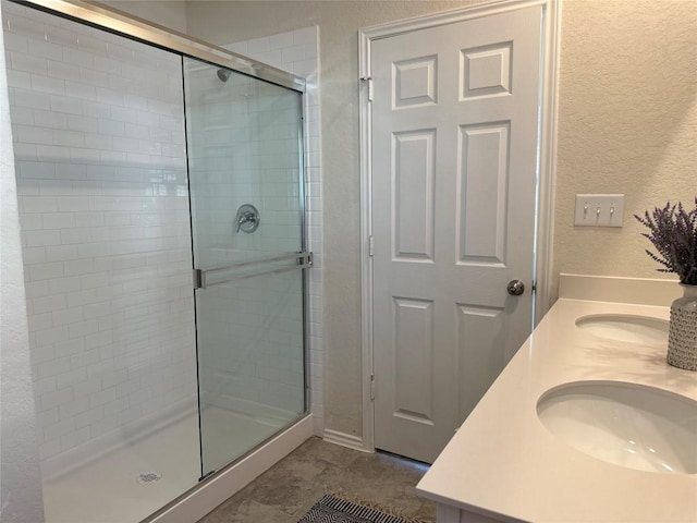 full bathroom featuring double vanity, a sink, a textured wall, and a stall shower