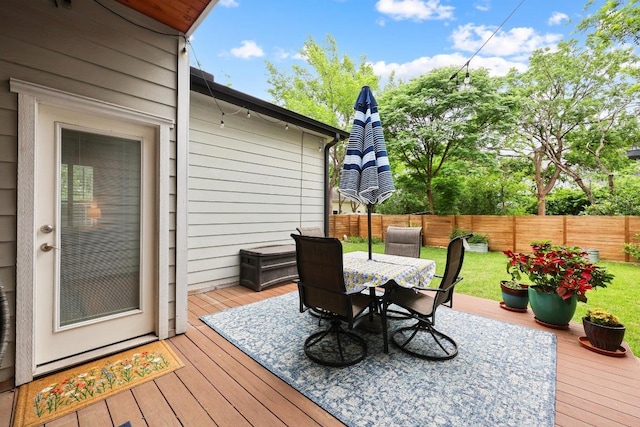 wooden terrace with a fenced backyard, outdoor dining area, and a yard