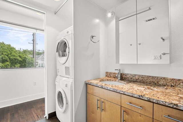 washroom with laundry area, a sink, stacked washing maching and dryer, dark wood-type flooring, and visible vents