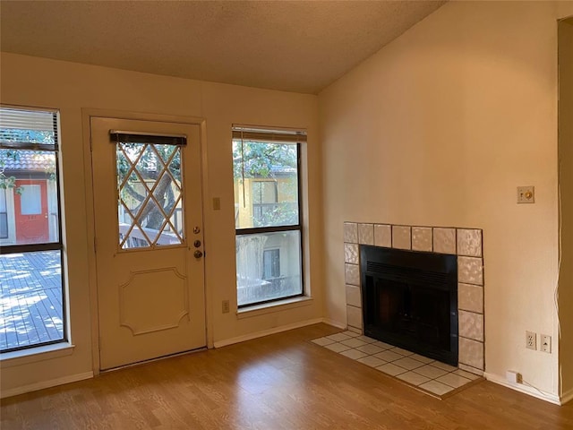 doorway to outside featuring baseboards, a fireplace, vaulted ceiling, and light wood-type flooring