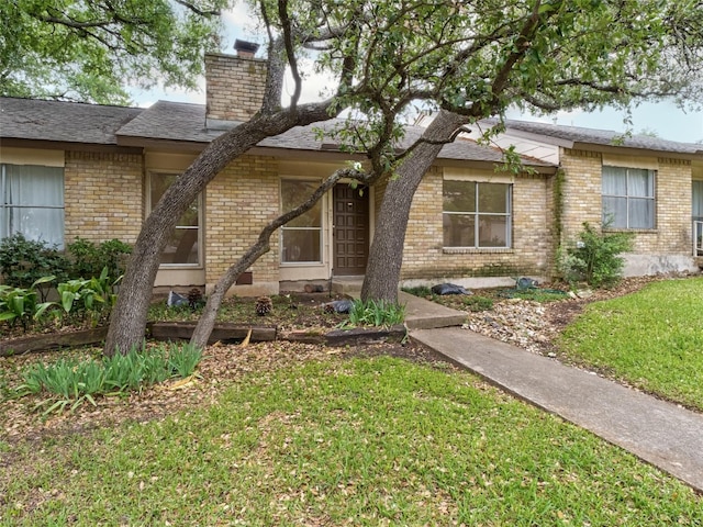 view of front facade featuring roof with shingles, a chimney, a front yard, and brick siding