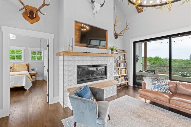 living area with a towering ceiling, a fireplace, baseboards, an inviting chandelier, and hardwood / wood-style floors