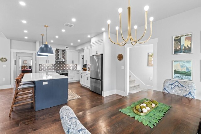 kitchen featuring white cabinets, an island with sink, wall chimney exhaust hood, stainless steel appliances, and decorative backsplash