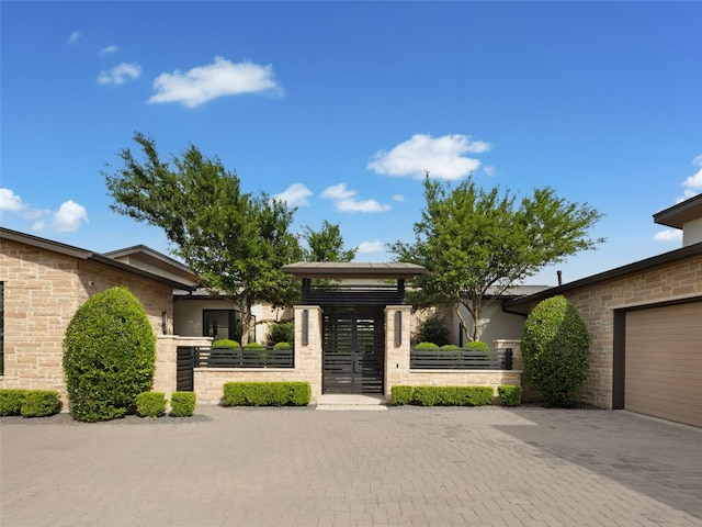 view of front of house featuring driveway, a fenced front yard, a gate, an attached garage, and stone siding