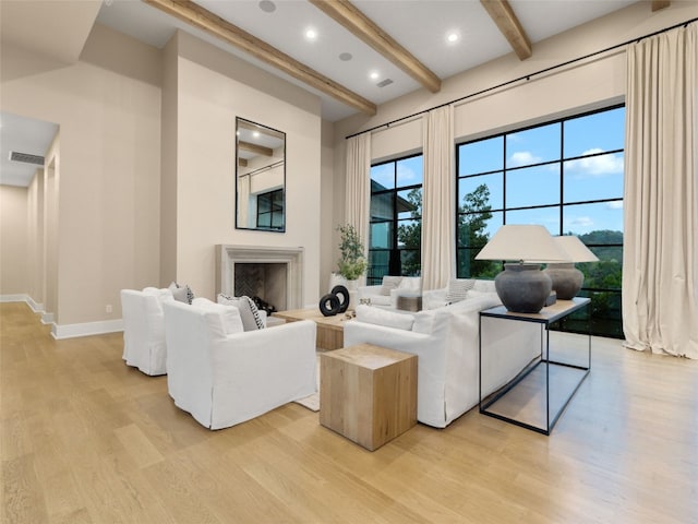 living room featuring visible vents, a fireplace, beamed ceiling, light wood-style floors, and a high ceiling