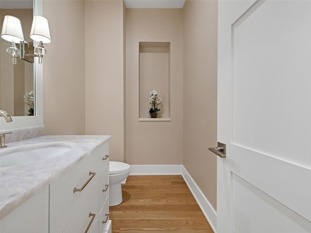 bathroom featuring vanity, baseboards, wood finished floors, and toilet