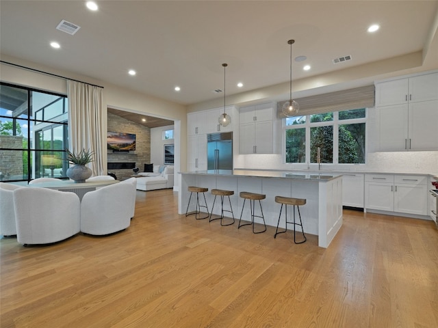 kitchen featuring visible vents, decorative backsplash, a kitchen breakfast bar, built in refrigerator, and light wood finished floors