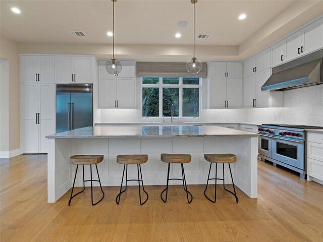 kitchen with visible vents, light wood-style floors, premium appliances, under cabinet range hood, and white cabinetry