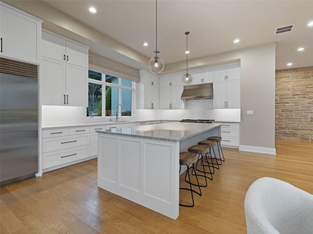 4701 Peralta Ln, Austin, TX 78735 - kitchen featuring stainless steel appliances, under cabinet range hood, a center island, white cabinets, and decorative backsplash