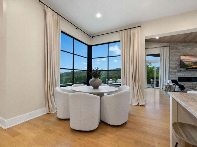 dining space featuring baseboards, light wood finished floors, a healthy amount of sunlight, and a fireplace