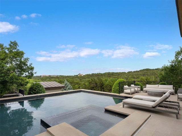 view of swimming pool with a wooded view, an outdoor hangout area, and a fenced in pool