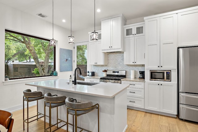 kitchen featuring visible vents, appliances with stainless steel finishes, a sink, light countertops, and an island with sink