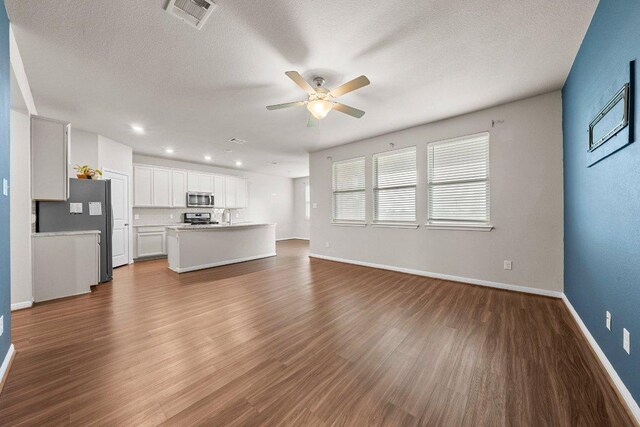unfurnished living room with ceiling fan, visible vents, baseboards, and dark wood-type flooring