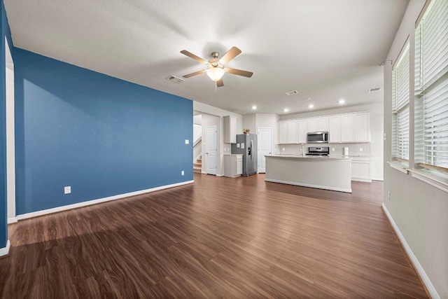 unfurnished living room with ceiling fan, baseboards, visible vents, dark wood-style floors, and stairway