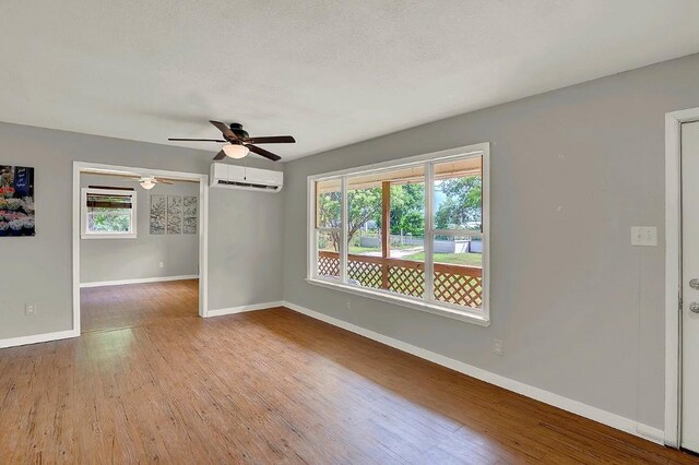 spare room featuring an AC wall unit, baseboards, wood finished floors, and a healthy amount of sunlight