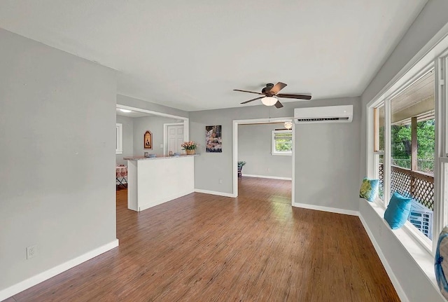 unfurnished living room featuring baseboards, a wall unit AC, a ceiling fan, and wood finished floors