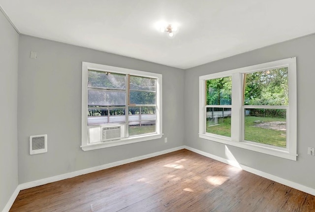 spare room with baseboards, wood finished floors, visible vents, and cooling unit