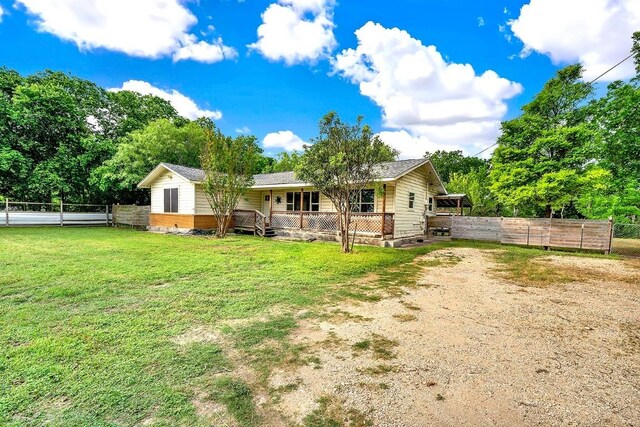 back of house featuring a lawn, a fenced backyard, dirt driveway, and covered porch