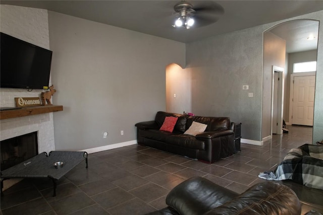 living room with dark tile patterned flooring, arched walkways, ceiling fan, and a fireplace