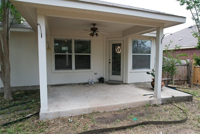 view of exterior entry with a patio, fence, and a ceiling fan