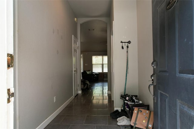 corridor featuring dark tile patterned floors, arched walkways, and baseboards