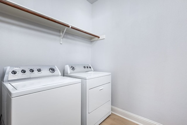 washroom with laundry area, baseboards, washer and dryer, and light wood-type flooring