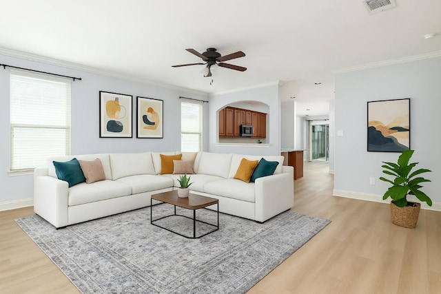 living room with visible vents, crown molding, baseboards, light wood-type flooring, and a ceiling fan