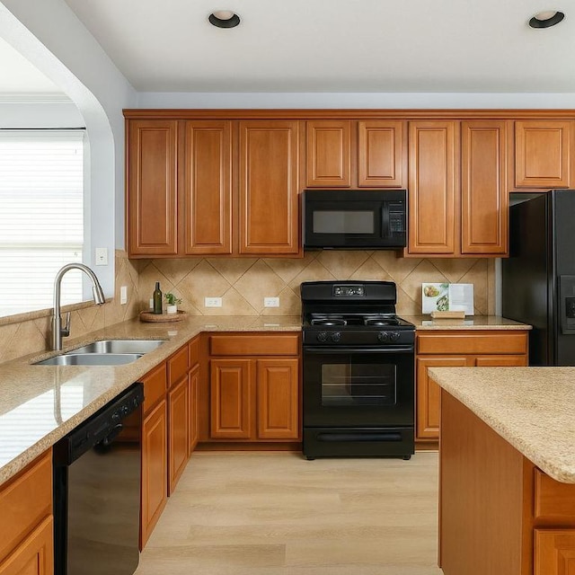 kitchen with a sink, brown cabinetry, black appliances, and light wood-type flooring