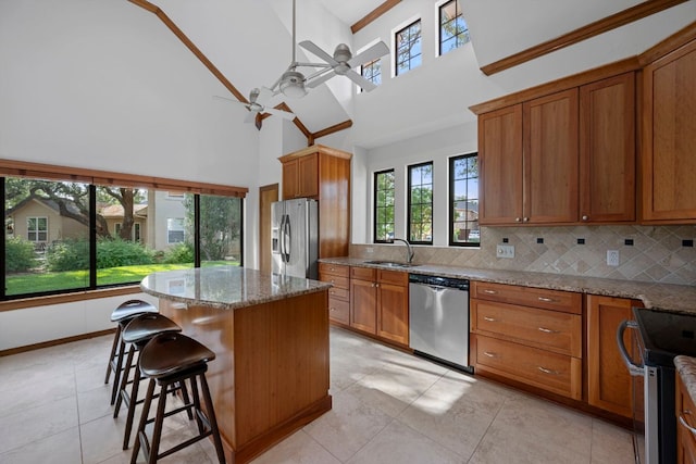 kitchen featuring ceiling fan, brown cabinetry, a kitchen island, a sink, and stainless steel appliances