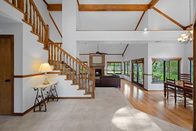 tiled foyer entrance with a lit fireplace, stairway, high vaulted ceiling, baseboards, and ceiling fan with notable chandelier