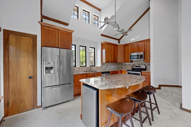 kitchen with appliances with stainless steel finishes, a center island, a ceiling fan, a towering ceiling, and backsplash