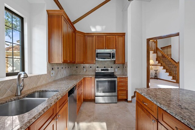 kitchen with a sink, appliances with stainless steel finishes, light stone countertops, and tasteful backsplash