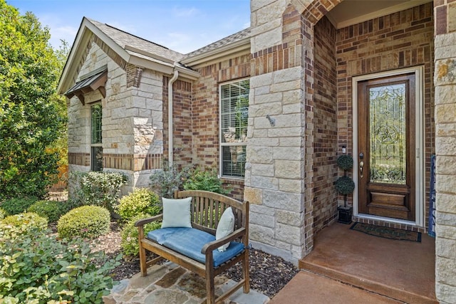 entrance to property featuring roof with shingles, brick siding, and stone siding