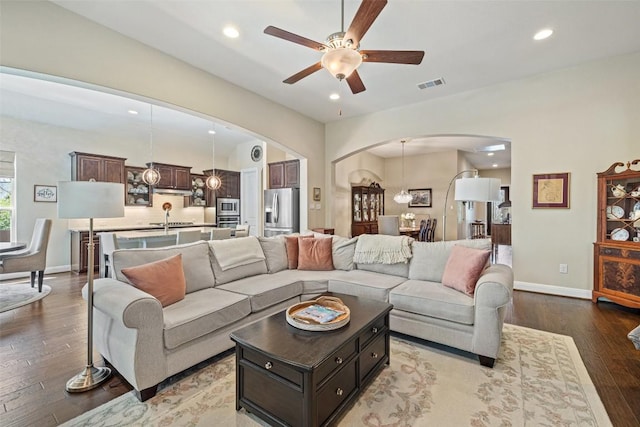 living area with arched walkways, visible vents, hardwood / wood-style flooring, and ceiling fan with notable chandelier