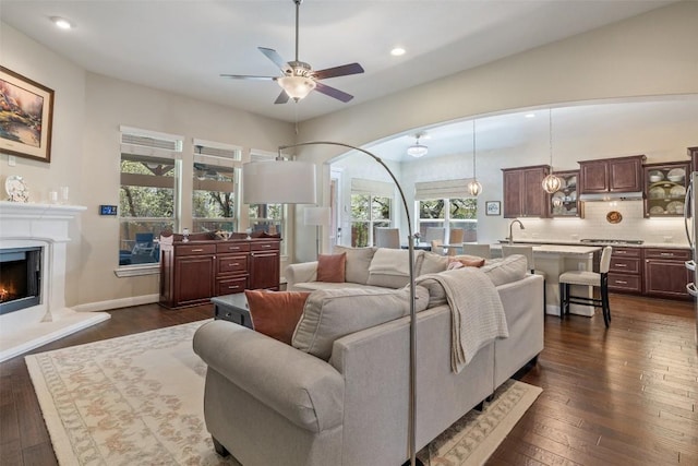 living room featuring recessed lighting, a ceiling fan, dark wood-type flooring, and a warm lit fireplace