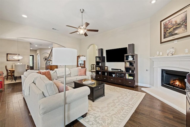 living area with ceiling fan, visible vents, arched walkways, a glass covered fireplace, and dark wood-type flooring