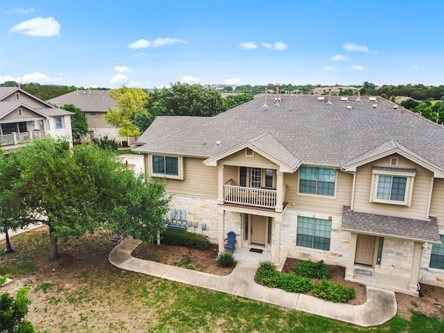 townhome / multi-family property with roof with shingles, a balcony, and stone siding