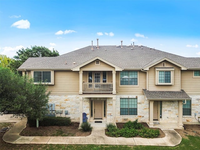 multi unit property featuring a shingled roof, stone siding, and a balcony