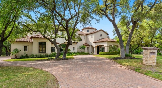 mediterranean / spanish-style house with curved driveway, a tiled roof, stucco siding, and a front yard