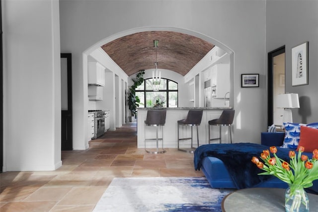 living area featuring arched walkways, vaulted ceiling, baseboards, stone tile flooring, and an inviting chandelier