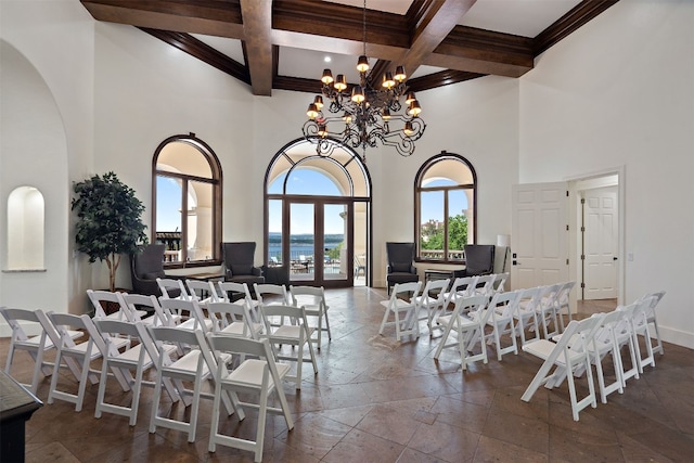 dining space with beam ceiling, a notable chandelier, stone tile flooring, and a towering ceiling